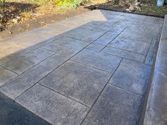 Freshly installed stamped concrete patio with a textured stone pattern adjacent to a garden bed.