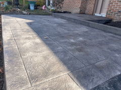 Stamped concrete driveway with a textured pattern leading to a front entrance with a raised concrete walkway and brick exterior wall.