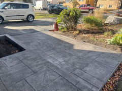 Gray stamped concrete walkway with a step beside garden landscaping and driveway