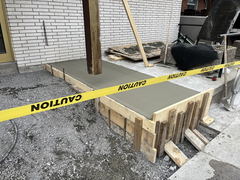 Freshly poured concrete porch with wooden forms, caution tape, and construction materials nearby