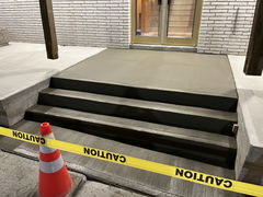Freshly poured concrete steps and landing in front of a building, blocked off with caution tape and a traffic cone.