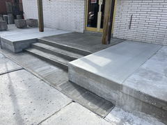 Freshly poured concrete steps and ramps leading to a commercial building entrance with a brick exterior.
