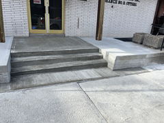 Freshly poured concrete steps with a ramp leading to double doors and a brick building facade