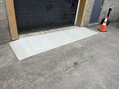 Freshly poured concrete ramp in front of a garage door with a traffic cone nearby
