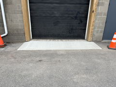 Freshly poured concrete ramp in front of a commercial garage door with two orange safety cones nearby