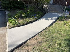 Freshly poured concrete walkway curving through a front yard garden leading to steps and a porch.