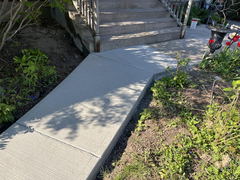 Freshly poured concrete walkway leading to a set of steps with garden beds on both sides.