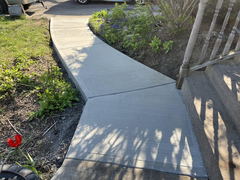 Freshly poured concrete walkway with control joints leading from front steps through landscaped yard to driveway