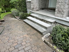 Freshly poured concrete steps leading to a front porch next to a stamped concrete walkway and landscaped garden shrubs