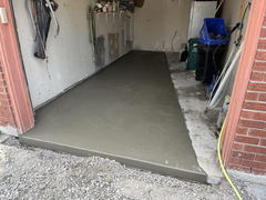 Freshly poured concrete garage floor slab with smooth finish adjacent to exposed gravel outside the garage entrance.