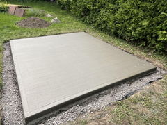 Freshly poured concrete slab with smooth broom finish surrounded by gravel and grass in a backyard setting.