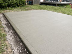 Freshly poured and brushed concrete slab with smooth edges surrounded by gravel and grass.