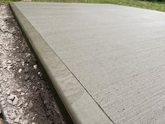 Freshly poured concrete slab with smooth finished edge and brushed surface next to gravel and soil.