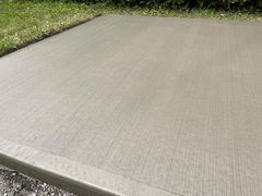 Freshly finished concrete slab with broom texture and smooth edges next to grass.