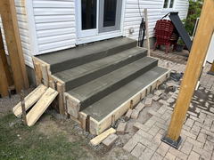 Freshly poured concrete steps with wooden forms next to a house patio and paver walkway.