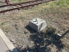 Concrete foundation with anchor bolts next to railway tracks on gravel and dirt ground