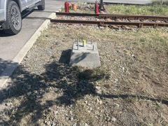 Concrete footing with anchor bolts installed near railway tracks and gravel parking area.