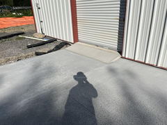 Freshly poured concrete driveway with a small ramp leading to a metal roll-up garage door on a metal building