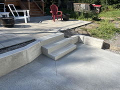 Concrete steps and retaining wall connecting a lower driveway area to a raised patio with paver stones and outdoor seating.
