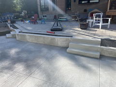 Stamped concrete driveway with a three-step concrete staircase leading to a raised patio with paver stones and outdoor furniture