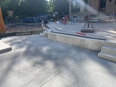Freshly poured stamped concrete driveway with a concrete retaining wall and steps leading up to a patio with pavers and outdoor seating.