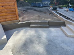 Freshly poured concrete steps and landing connecting a patio to a gravel area, with construction tools and a blue dumpster in the background.