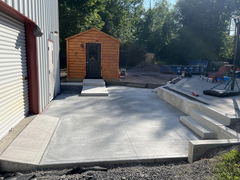 Freshly poured concrete patio with steps, walkway, and a small wooden shed in the background.