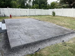 Stamped concrete patio with ashlar slate pattern surrounded by gravel in a fenced backyard.