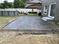 Freshly installed stamped concrete patio with a border of gravel beside a house and steps leading to a sliding glass door.