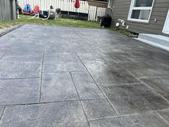 Stamped concrete patio with a slate pattern beside a house and concrete steps, backyard furniture in the background.