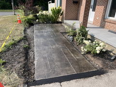Freshly installed stamped concrete walkway leading to a porch, bordered by flower beds and marked with caution tape and traffic cones.