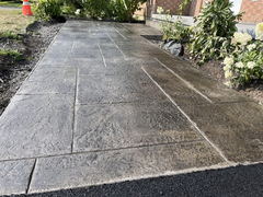 Stamped concrete walkway with a textured pattern beside landscaped garden beds and a brick house