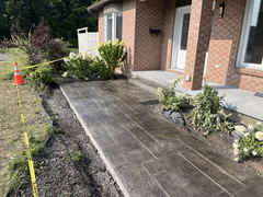 Stamped concrete walkway leading to a brick house entrance, surrounded by caution tape and landscaping.