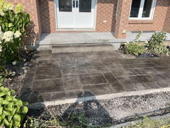 Stamped concrete walkway with a single step leads to a front porch of a brick house, bordered by flower beds.