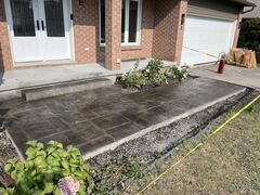 Stamped concrete walkway with step in front of brick house and garage, bordered by caution tape and garden beds.