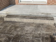 Stamped concrete patio with a single concrete step leading to a smooth concrete porch in front of a brick house.