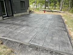 Freshly installed stamped concrete patio with a geometric pattern beside a modern house.