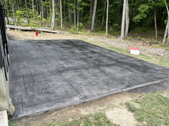 Freshly poured dark stamped concrete patio with rectangular pattern next to a wooded area.