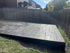 Freshly installed stamped concrete patio with a raised edge in a fenced backyard