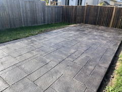 Stamped concrete patio with a slate pattern set in a backyard, bordered by wooden fencing and grass.