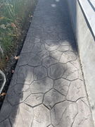 Stamped concrete walkway with irregular stone pattern alongside a building and chain link fence.