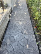 Stamped concrete walkway with irregular stone pattern beside wooden steps and a garden fence.