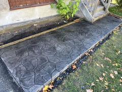 Dark gray stamped concrete walkway with a stone pattern beside a wooden porch and garden edging