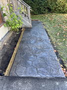 Textured stamped concrete walkway beside wooden porch steps and garden bed