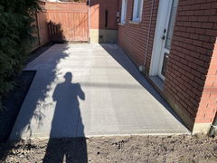 Freshly poured concrete patio beside a red brick house with a wooden fence in the background.