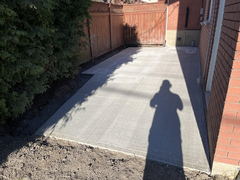 Newly poured and finished concrete patio beside a brick house with a wooden fence in the background.