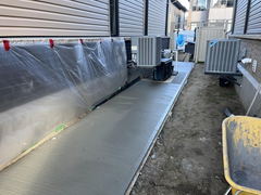 Freshly poured concrete walkway between two buildings with air conditioning units and protective plastic sheeting on the wall.