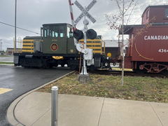 Railroad crossing with a green and yellow locomotive and red caboose next to a concrete sidewalk and metal crossing signal.