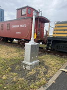 Metal utility box mounted on concrete base beside railway tracks with red Canadian Pacific caboose in background