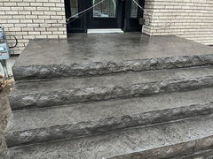 Stamped concrete front steps and landing with a textured stone pattern leading to a black double door entrance on a brick house.